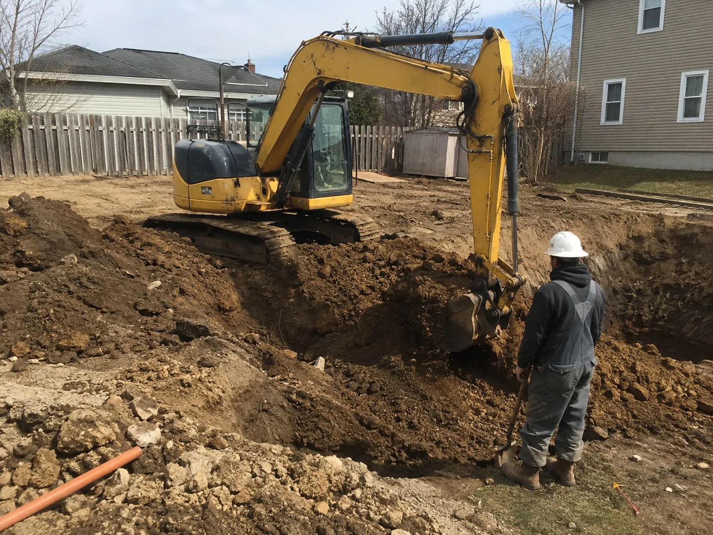 Excavator digging out a residential site while a worker trims the excavation by hand