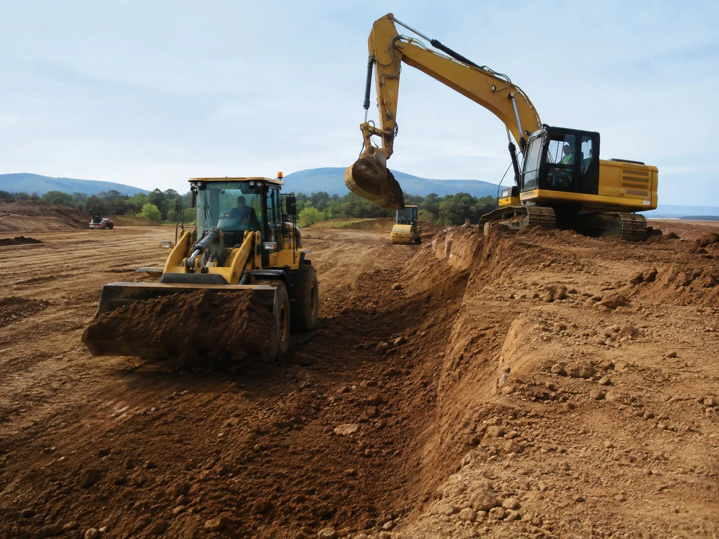 Excavator and wheel loader moving earth across a large site being cut to level